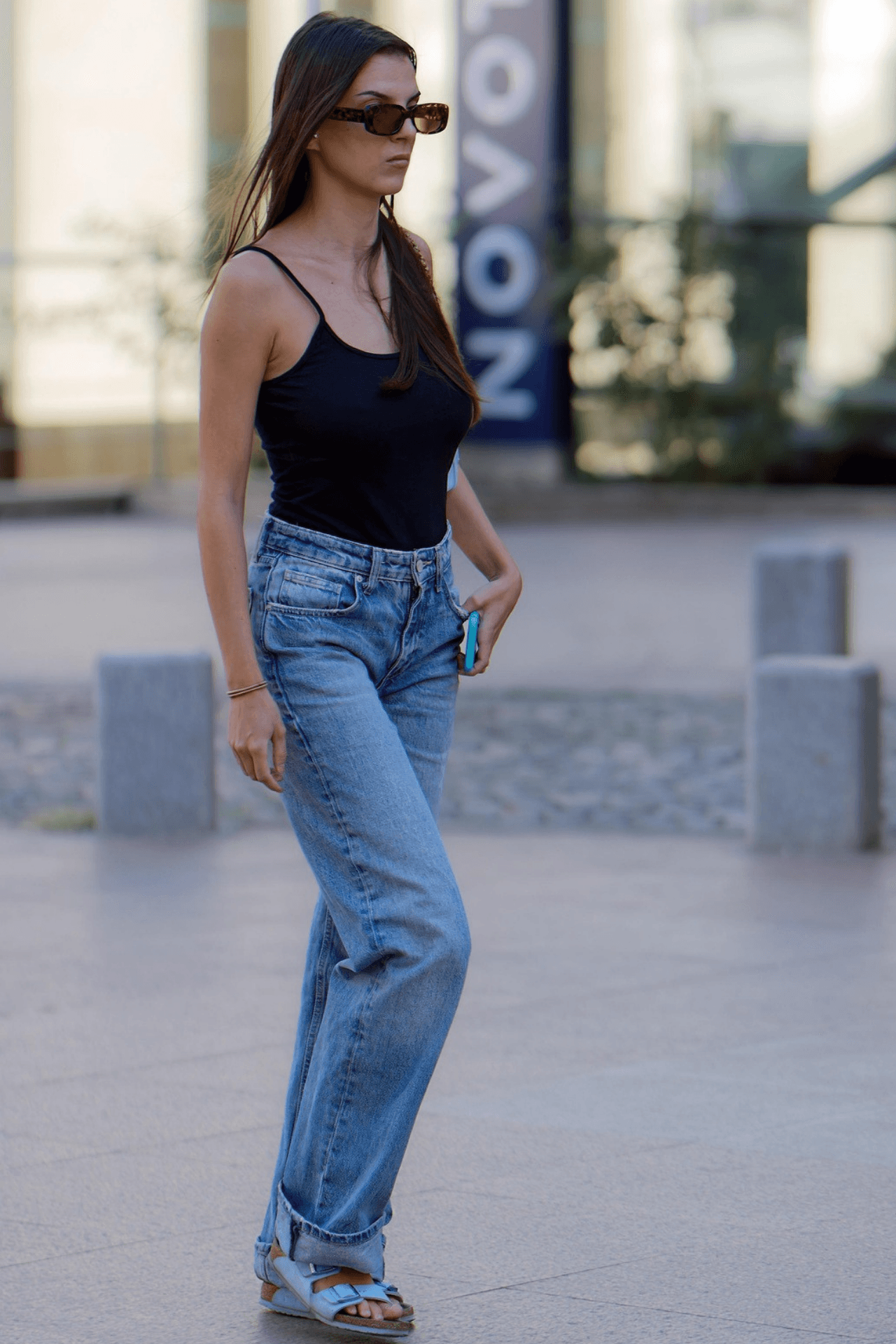 Woman wearing straight-leg vintage jeans, a black tank top, and sandals – timeless denim trend for spring 2025.