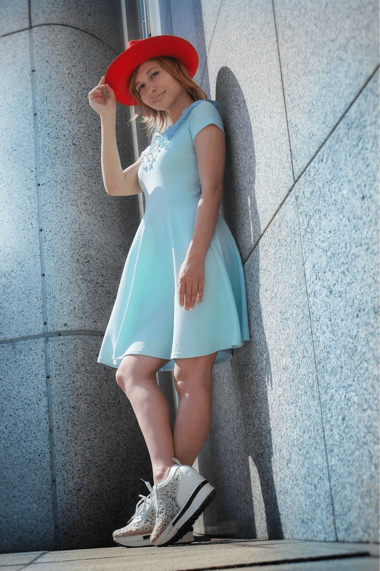 Woman wearing a mint green skater dress, white sneakers, and a bold red hat – playful pastel fashion trend for spring 2025.