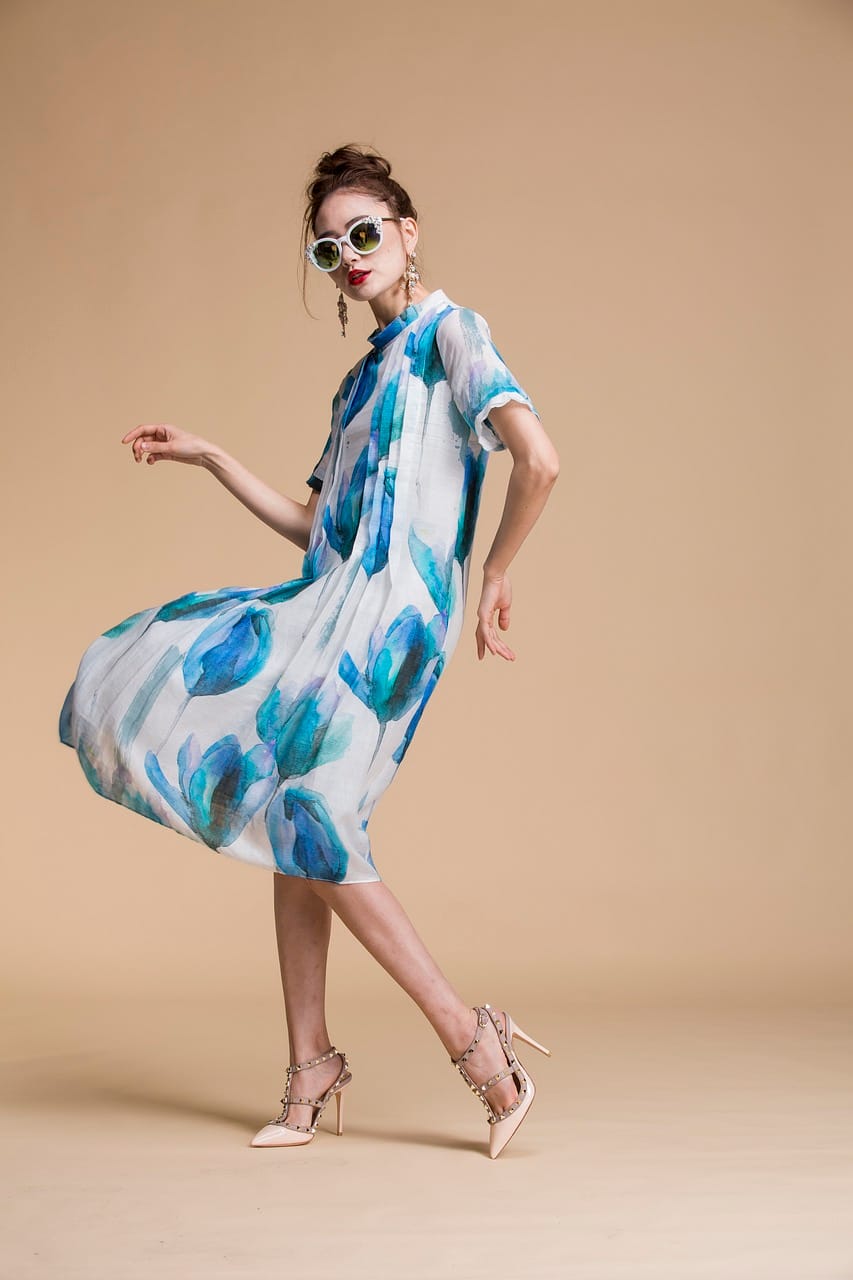 Model wearing a white flowy midi dress with bold blue floral print and nude heels – stylish statement piece for spring 2025 fashion trends.