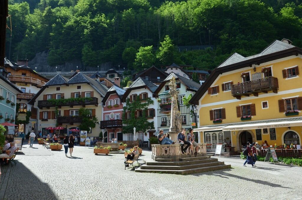 Colorful traditional buildings and central square with people relaxing around the fountain in Hallstatt, Austria