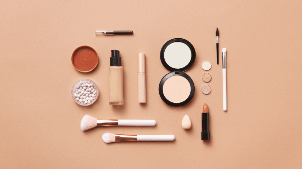 Flatlay of a minimal makeup kit with foundation, powder, brushes, lipstick, eyeshadow, and beauty tools – travel-friendly beauty essentials.