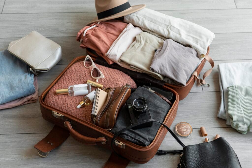Stylish travel essentials laid out in and around an open suitcase, including clothes, accessories, and a camera