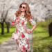 Fashionable woman wearing floral dress and accessories, walking through a spring park with blooming trees