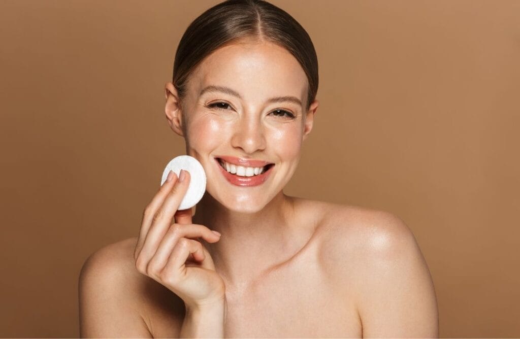 Woman smiling while gently cleansing her face as part of a minimalist skincare routine