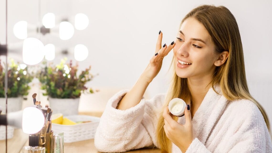 Woman applying moisturizer during minimalist skincare routine at vanity
