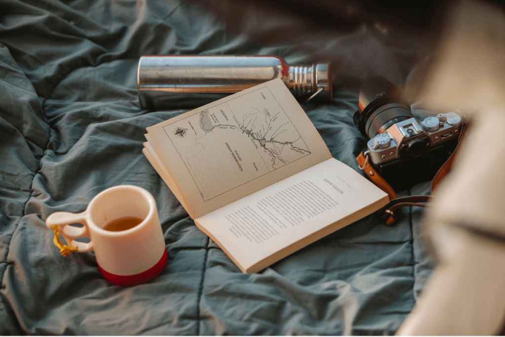 Open book, camera, and cup of tea on a blanket during a peaceful camping morning