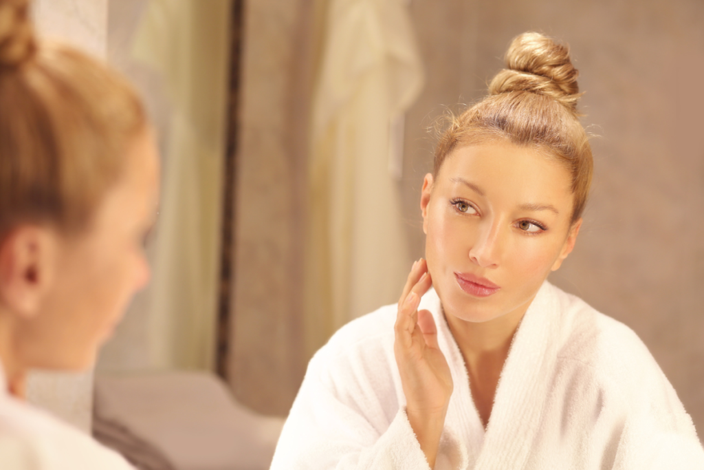 Woman in white robe gently touching her face, reflecting quietly after her self-care routine