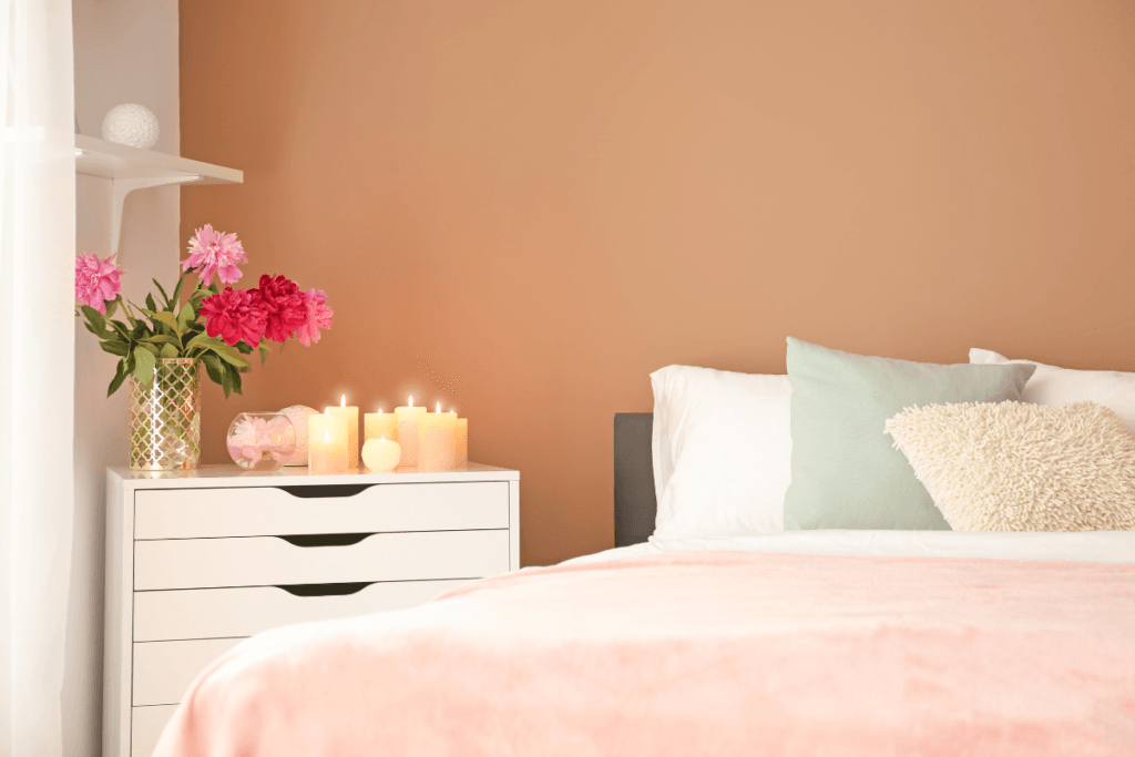 bedside table with glowing candles, flowers and pastel decor – feminine home lighting idea