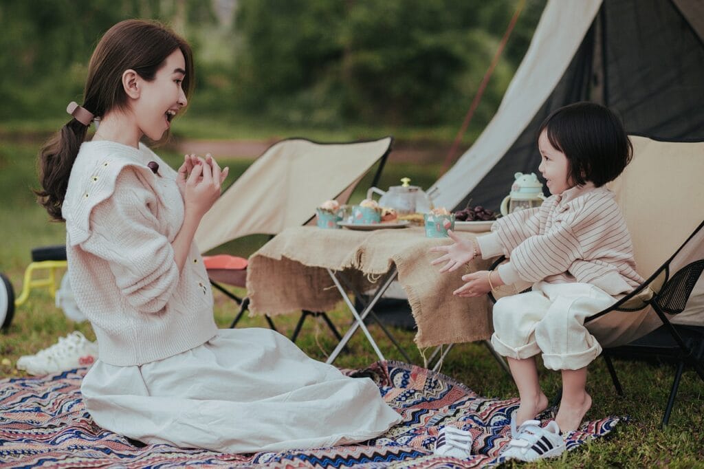 Mother and child enjoying a picnic together while camping outdoors, smiling and playing near a tent