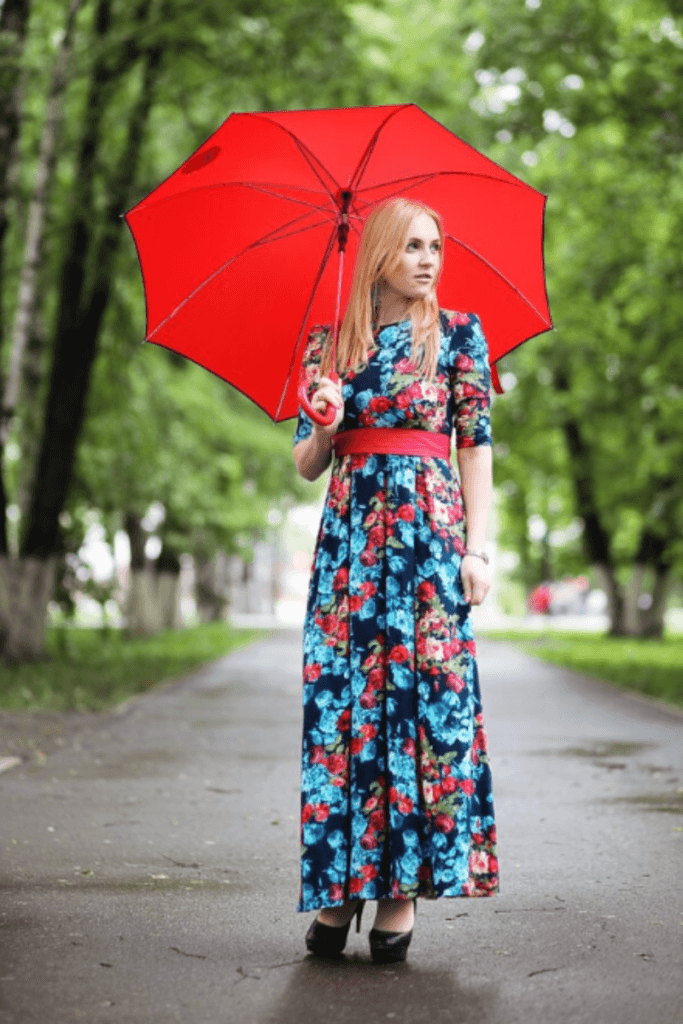 Woman wearing a floral maxi dress and holding a red umbrella – stylish rainy summer day outfit