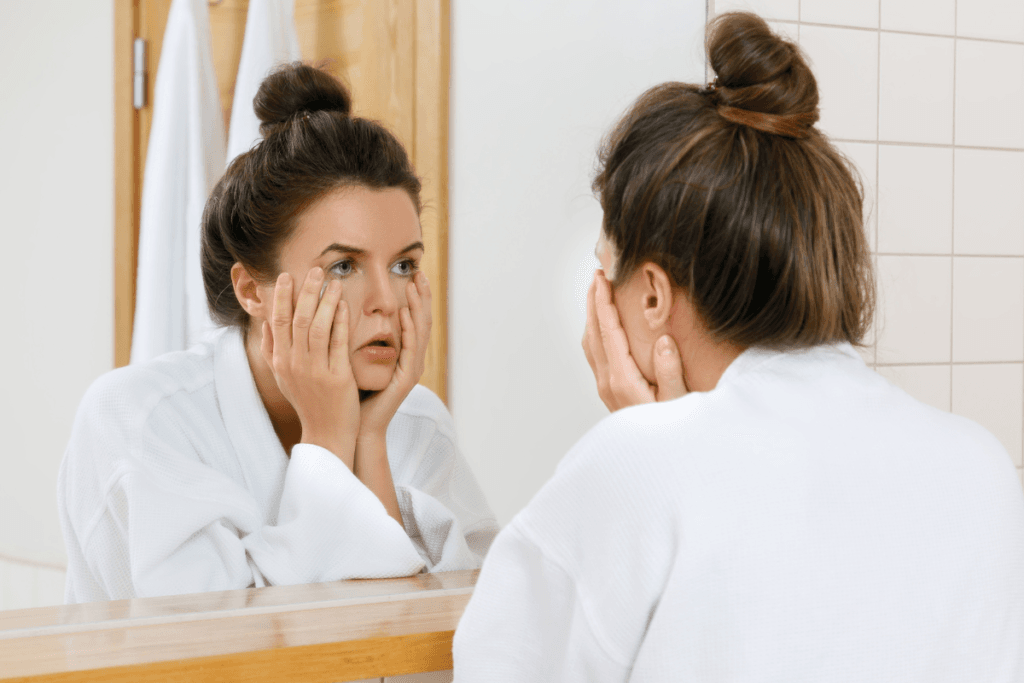 Tired woman in robe looking at herself in the mirror before starting her self-care routine