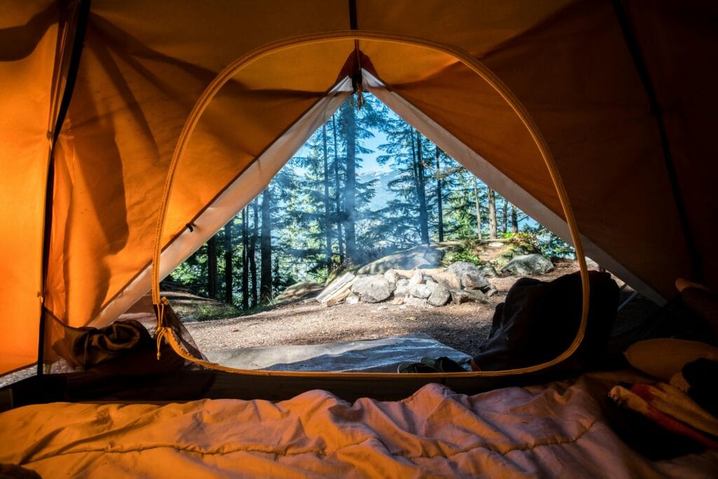 Inside view from a cozy tent looking out at a forest and a campfire, with blankets and a peaceful morning light