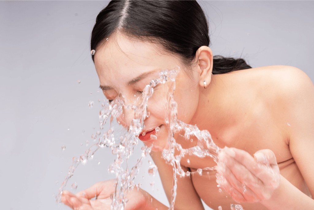 Young woman splashing water on her face during cleansing routine – fresh skincare step