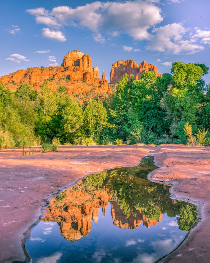 Cathedral Rock reflected in water puddle at Crescent Moon Picnic Site, Sedona, under a bright blue sky