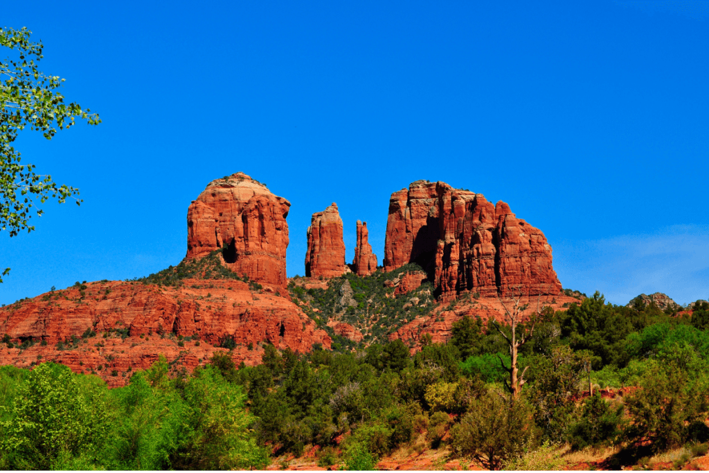 Cathedral Rock in Sedona under a clear blue sky with lush greenery in the foreground