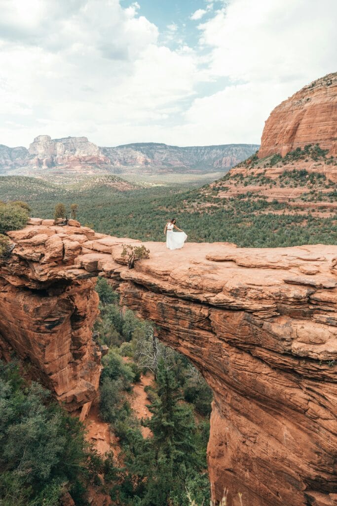 Woman standing on Devil’s Bridge in Sedona, surrounded by red rock formations and vast desert landscape.