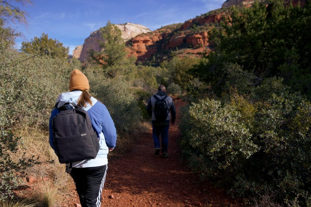 Hikers on a red rock trail surrounded by desert vegetation in Sedona.